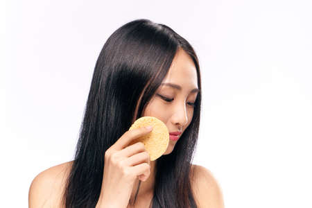 Woman rubs her face sponge on isolated background portrait.の写真素材