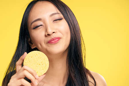 Beautiful, facial, young woman with a sponge, cleans the face of the sponge on a yellow background.の写真素材