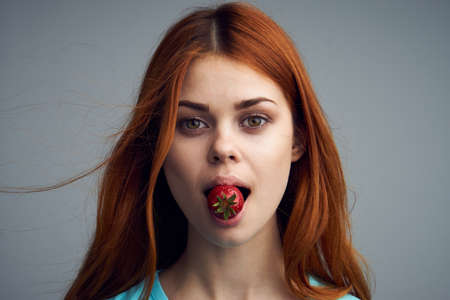 A woman holding a strawberry in her mouth, a strawberry sweet on a gray background.