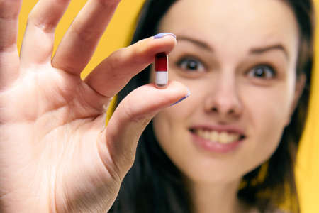 Woman sick, woman with pill, woman on yellow background portrait.