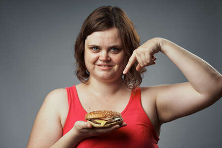 Tasty, woman shows a hamburger, a woman with a hamburger on a gray background, meal.