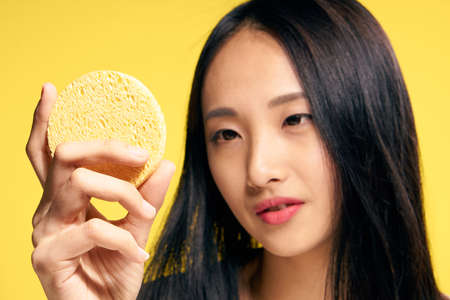Woman looking at a sponge, looking after a face, woman on a yellow background.の写真素材