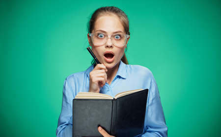 Surprised woman, woman with glasses, woman with a notebook and pen on a green background.