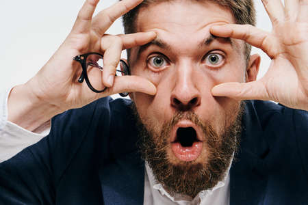 Business man widened his eyes with his hands, businessman holds glasses, businessman on a light background portrait.の写真素材