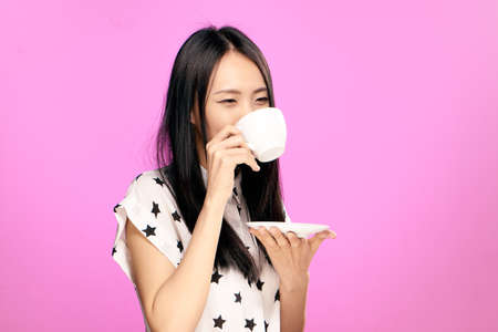 Asian, girl drinks tea, girl on pink background, woman holds mug.の写真素材