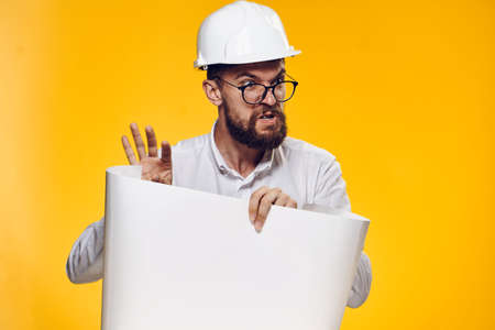 Engineer, builder, helmet, engineer swears, a builder holds a blueprint, a builder is dissatisfied, a man on a yellow background.の写真素材