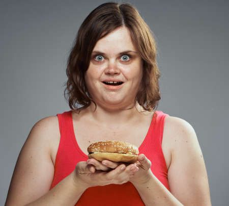 Fast food, slimming, hamburger, a woman holding a hamburger, a woman on a gray background.の写真素材