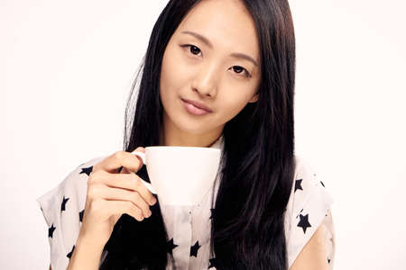 Asian girl holding a mug, a girl drinking tea, a woman drinking coffee, a woman on a white background, a woman on an isolated background.の写真素材