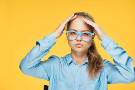 Woman with glasses, woman on yellow background, woman holds on to head.