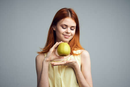 Diet, fruit, girl holding an apple on a gray background, beautiful young woman with red hair.の写真素材