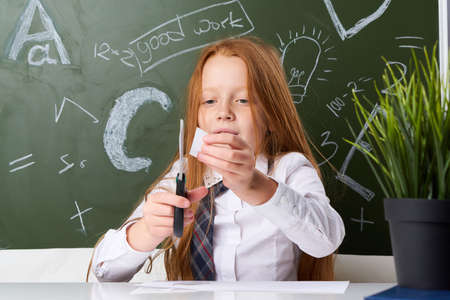 Schoolgirl cuts out paper sitting at a desk, classroom, school, student, study, child.の写真素材