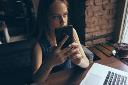 Woman in a cafe behind a laptop holds a phone, business, work.の写真素材