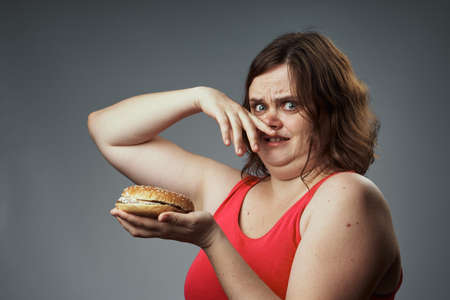 Harmful food, hamburger, hamburger stinks, woman with a hamburger, woman on a gray background.
