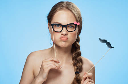 Accessories on a stick, a woman with glasses and a mustache on a stick, a holiday, not a happy woman, a woman on a light background.の写真素材