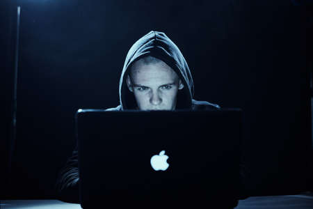 A hacker in a hood, a hacker breaks into computer networks, a hacker on a dark background.の写真素材