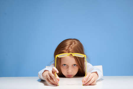 The child at the table is holding glasses, the little girl is on a blue background,schoolgirl.の写真素材