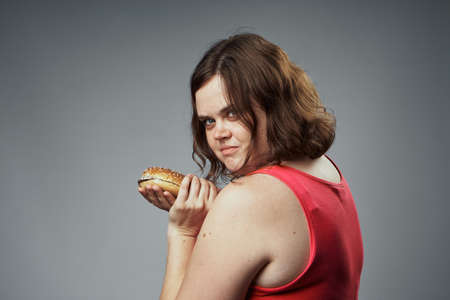 Diet, fat woman holding a hamburger on a black background, fast food, health, proper nutrition.