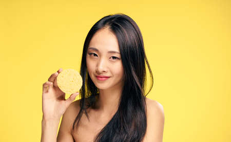 Asian, woman on yellow background, make-up sponge, brunette, cosmetics.の写真素材