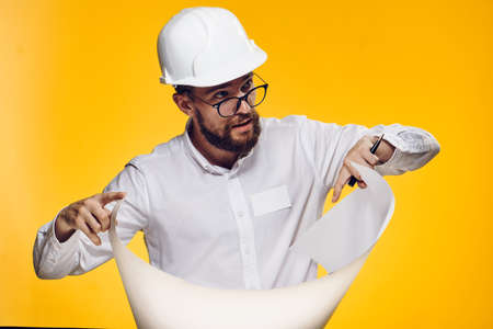 Engineer with a beard holds a blueprint on a yellow background, emotions, a builder.の写真素材