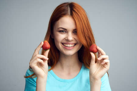 Smile, laugh, berries, woman on a gray background holds a strawberry, summer.の写真素材