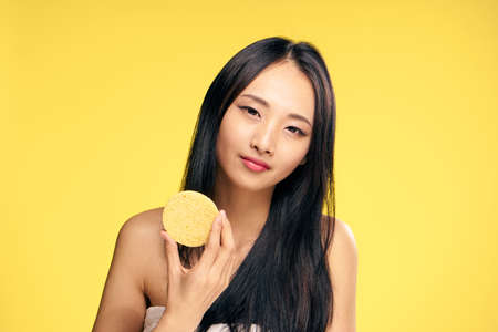 Asian, woman on yellow background holds a sponge for make-up removal, beauty.の写真素材