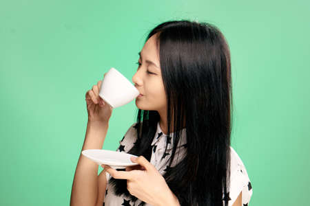 Asian, woman on green background drinking tea, coffee, holding mug.