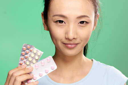 Asian woman on a green background holds a pill.の写真素材