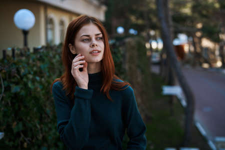Beautiful young woman with red hair walking along the street.