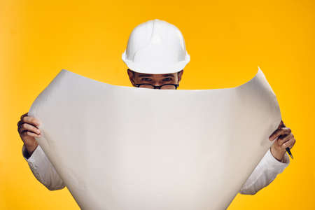 Engineer with a beard on a yellow background holds a drawing.の写真素材