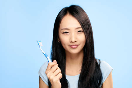 Asian woman on a blue background holds a toothbrush.の写真素材