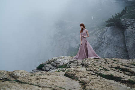 Beautiful young woman in a long dress in the mountains on a cliff.の写真素材