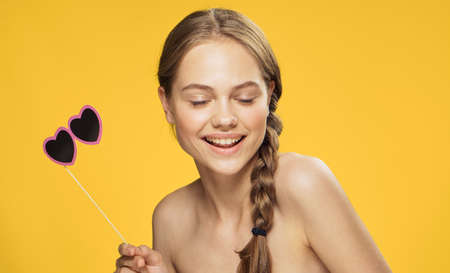 Beautiful young woman on a Yellow background holds paper accessories for parties.