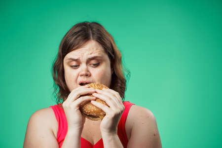 Fat woman on a green background eating a hamburger, fast food.の写真素材