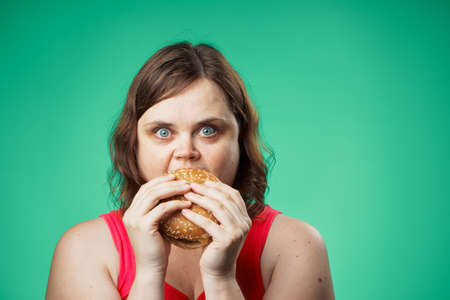Fat woman on a green background eating a hamburger, fast food.の写真素材
