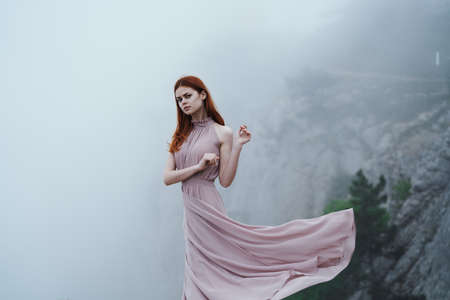 Beautiful young woman in a long dress in the mountains on a cliff.の写真素材