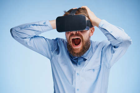 A young guy with a beard on a blue background with virtual reality glasses.