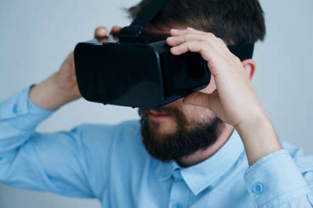 A young guy with a beard on a light background in virtual reality glasses.