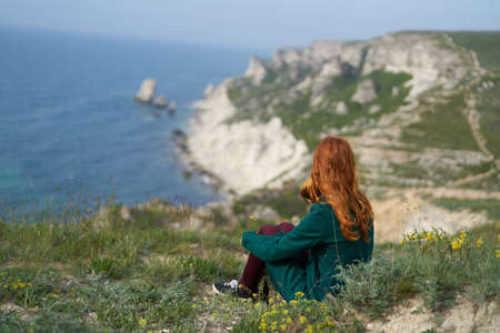 Beautiful young woman sitting on a cliff on a mountain above the sea.