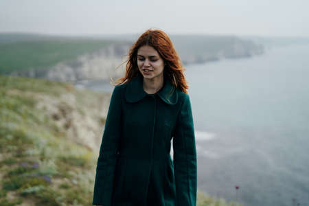 Beautiful young woman standing on a cliff of a mountain near the sea.