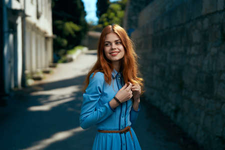Beautiful young woman in a blue dress walking along the boulevard in the city.の写真素材
