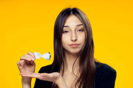 Beautiful young woman on a yellow background holds a paper bowtie.の写真素材