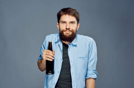 A young guy with a beard on a gray background holds a bottle of beer, alcohol.の写真素材