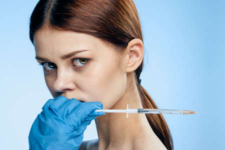 Young beautiful woman on a blue background holds a syringe, medicine, nurse.の写真素材