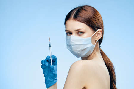 Young beautiful woman on a blue background holds a syringe, medicine, nurse.の写真素材