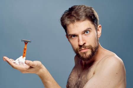 A young guy with a beard on a gray background applies a shaving foam.の写真素材