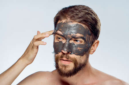 A young guy with a beard on a white isolated background is applying a clay facial mask.の写真素材
