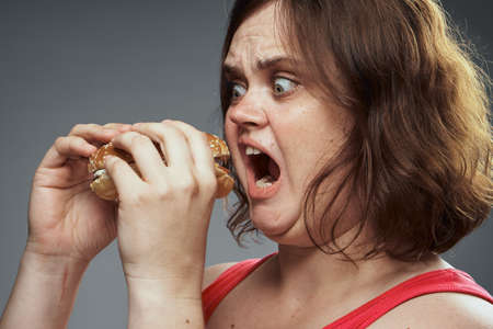 Fat woman on a gray background holds a hamburger.の写真素材