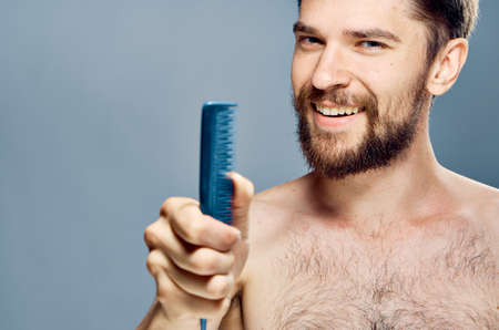 A young guy with a beard on a gray background holds a comb.の写真素材