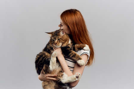 Beautiful young woman running on a light background holding a cat.の写真素材