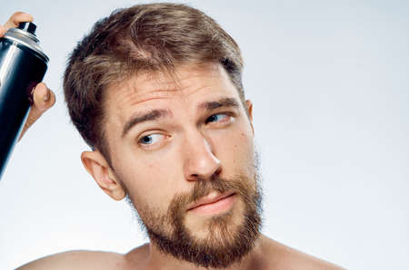 Young guy with a beard on a white isolated background purrs a hair spray.